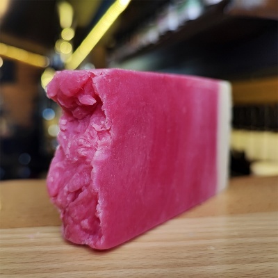 Barra de sabonete cor-de-rosa com textura rugosa numa das extremidades sobre superfície de madeira