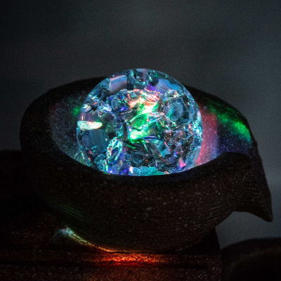 Esfera de vidro com cristais coloridos num suporte escuro com iluminação multicolor