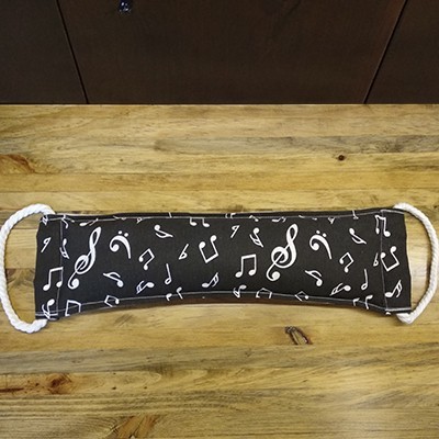 Máscara facial preta com notas musicais brancas e alças de corda branca sobre mesa de madeira