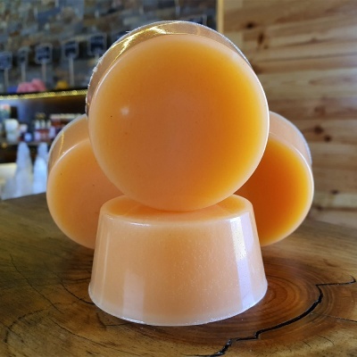 Sabonetes redondos laranja translúcidos sobre base de madeira em ambiente interno.