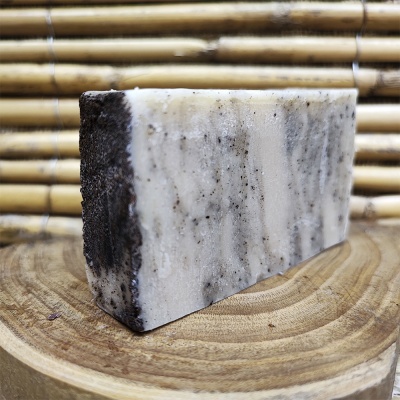Barra de sabão branco e cinza sobre disco de madeira com fundo de bambu