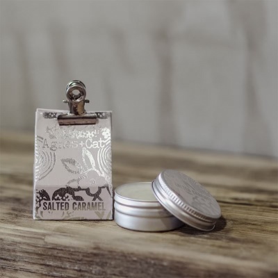 Vela perfumada em frasco metálico prateado junto a cartão prateado com texto SALTED CARAMEL