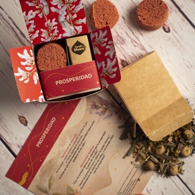 Caixa vermelha decorativa com incenso e disco castanho, saco de papel com ervas e folheto numa mesa de madeira