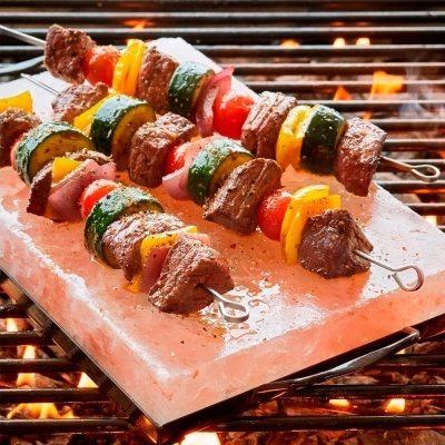 Espetos de carne e legumes grelhados numa placa de sal grosso cor de rosa sobre grelha a carvão