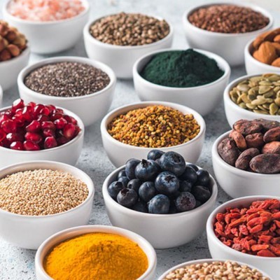 Tigelas brancas com sementes, frutos secos e especiarias coloridas sobre superfície cinza