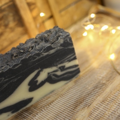 Barra de sabão artesanal preta e branca com textura sobre tecido e madeira