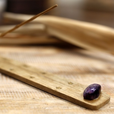 Suporte de incenso em madeira clara com pedra roxa e livro aberto desfocado
