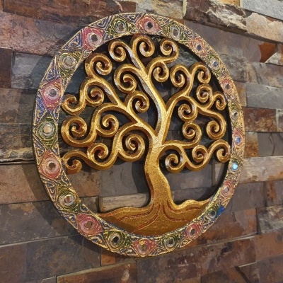 Escultura metálica dourada de árvore da vida com moldura colorida numa parede de pedra