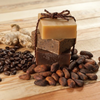 Três sabonetes empilhados com grãos de café, cacau e gengibre numa mesa de madeira