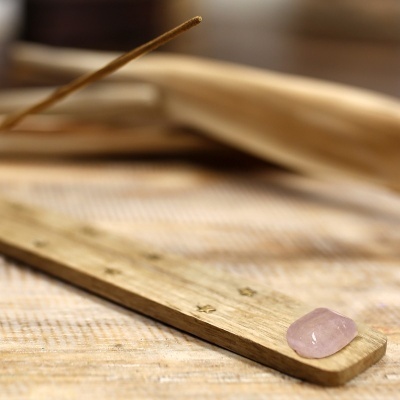 Incensário de madeira clara com pedra rosa sobre tecido bege
