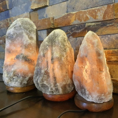 Três lâmpadas de sal do Himalaia iluminadas em bases de madeira com parede de pedras atrás