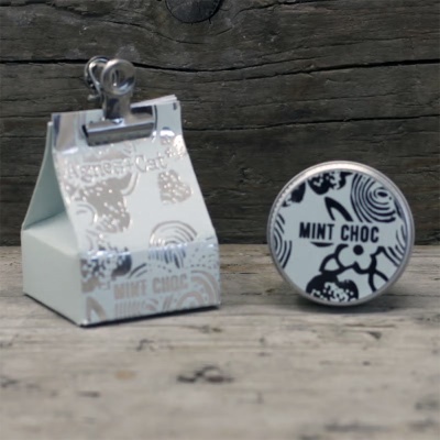 Caixa de cartão e objeto redondo com texto MINT CHOC sobre mesa de madeira.