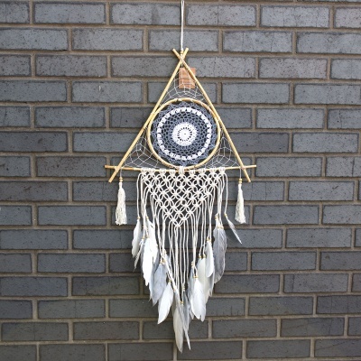 Pendurador de parede triangular com crochet e penas em fundo de parede de tijolos cinzentos