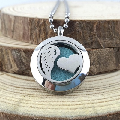 Colar com pendente redondo de metal prateado com asa e coração sobre fundo azul, exposto em troncos de madeira.