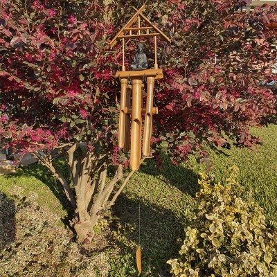 Sino dos ventos em madeira pendurado numa árvore com folhas vermelhas e arbustos ao redor