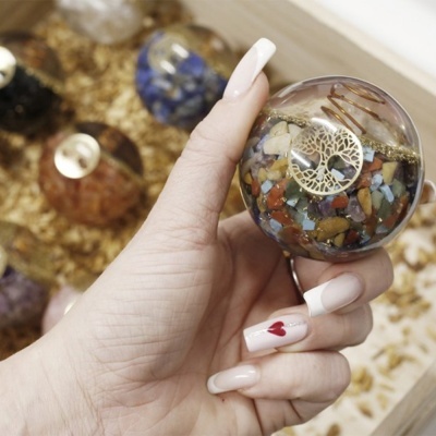 Mão segurando esfera decorativa de resina com pedras coloridas e pendente de árvore da vida