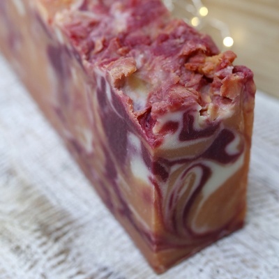 Barra de sabão artesanal marmoreada em castanho, creme e lilás, textura irregular no topo, sobre tecido branco