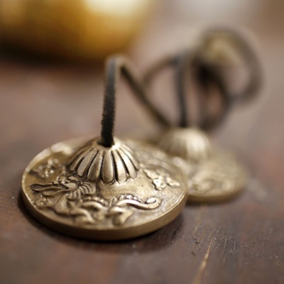 Par de címbalos tibetanos pequenos em metal dourado com cordas pretas sobre madeira