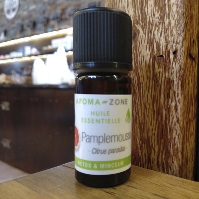 Frasco pequeno de óleo essencial com rótulo branco com texto verde e preto sobre superfície de madeira