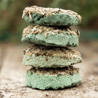 Quatro sabonetes artesanais verdes com ervas secas empilhados sobre madeira rústica