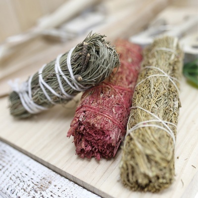 Três feixes de ervas secas amarrados com fio branco sobre tábua de madeira.