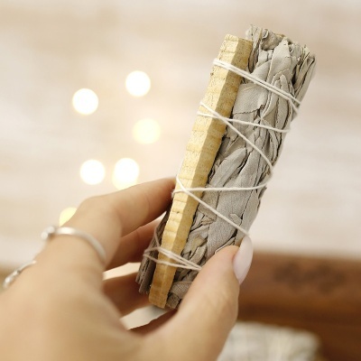 Mão segura incenso de folhas secas e madeira amarrados com fio branco em fundo desfocado