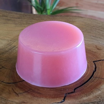 Sabonete rosa redondo sobre base de madeira com planta ao fundo