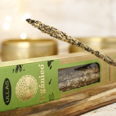 Incenso orgânico Ullas em embalagem verde com vara acesa sobre madeira