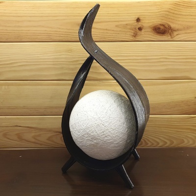 Escultura em ferro preto com esfera branca sobre mesa de madeira