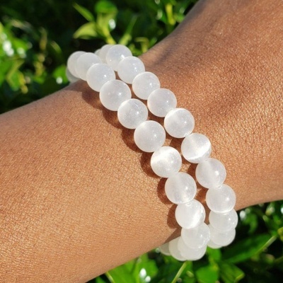 Pulseira elástica com contas redondas translúcidas brancas num pulso com fundo de folhas verdes