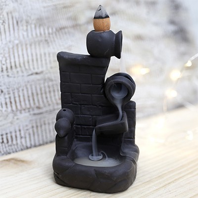 Escultura decorativa preta de cerâmica com chaminé e jarro vertendo fumo, sobre madeira clara