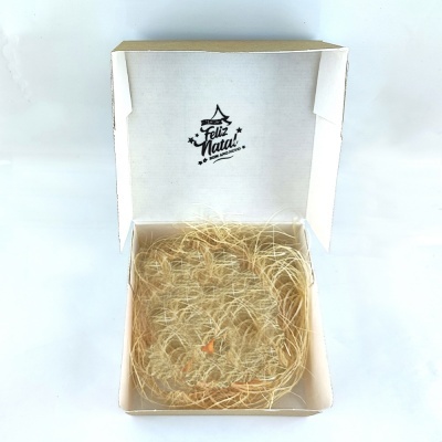 Caixa branca aberta com mensagem Feliz Natal e enchimento de palha seca