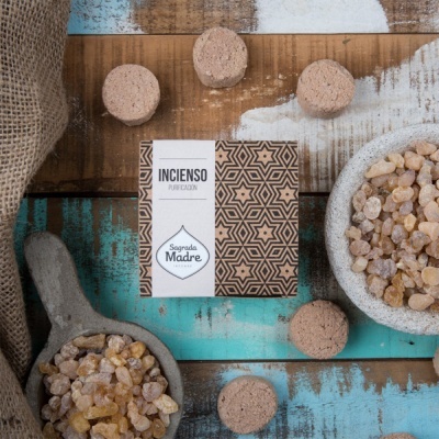 Caixa de incenso Sagrada Madre com rótulo branco e padrão geométrico castanho, rodeada por resina e queimadores de incenso