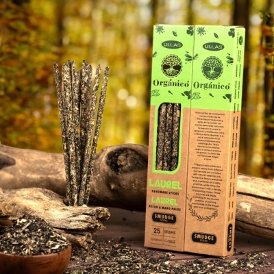Incensos naturais em sticks smudge da marca ULLAS com embalagem verde e castanha e sticks junto a peças de madeira em ambiente natural.