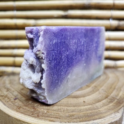 Sabonete artesanal roxo e branco com textura rústica sobre suporte de madeira