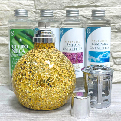 Lâmpada catalítica dourada com três frascos de recarga de fragrâncias em fundo branco