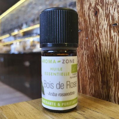 Frasco de óleo essencial Aromazone Bois de Rose sobre superfície amarela e fundo de madeira