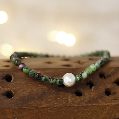 Pulseira com contas verdes e roxas em pedra natural e uma conta branca tipo pérola sobre superfície de madeira