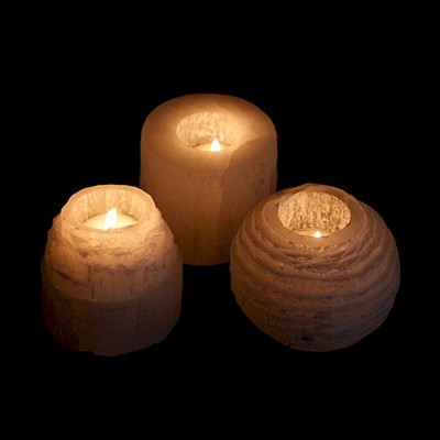 Três castiçais brancos com velas acesas sobre fundo escuro.