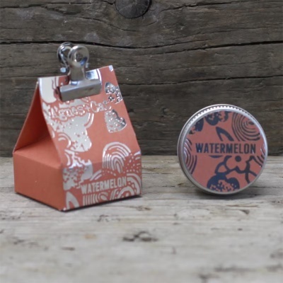 Embalagem laranja com decoração prateada e lata metálica com tampa decorada laranja e azul com texto WATERMELON