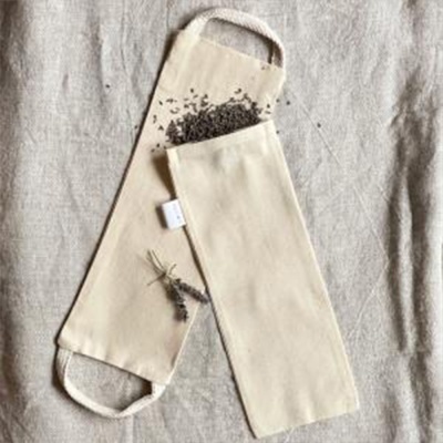 Dupla de bolsas de tecido cru com sementes e ramo seco sobre tecido claro