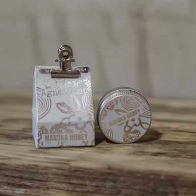 Embalagem branca e lata pequena decoradas em cobre com texto MANUKA HONEY