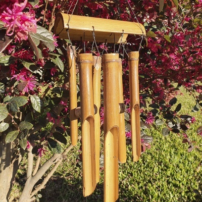 Carrilhão de vento de bambu pendurado num arbusto com flores cor-de-rosa.