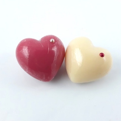 Dois chocolates em forma de coração, vermelho e branco, com pequenos detalhes metálicos.
