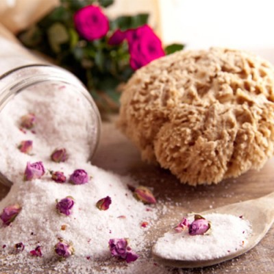 Sal branco com botões de rosa secos, colher de madeira, frasco de vidro e esponja natural sobre superfície de madeira