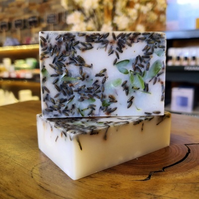 Sabonetes artesanais brancos com partículas marrons e folhas verdes sobre mesa de madeira