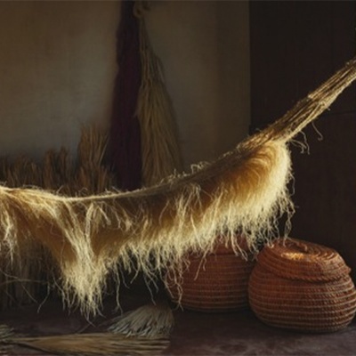 Rede artesanal de fibras naturais suspensa com cestos de palha ao fundo
