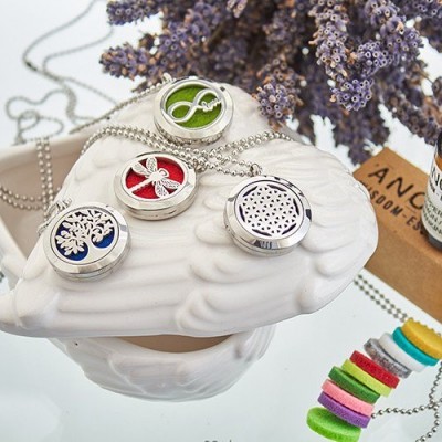 Quatro colares com pendentes redondos coloridos sobre peça branca decorativa com flores roxas ao fundo