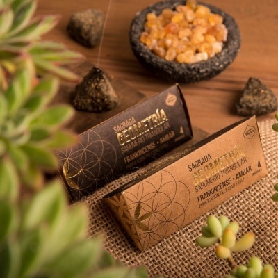 Incenso em cones e caixas com texto SAGRADA GEOMETRIA sobre superfície de madeira e tecido