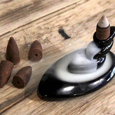 Base de incenso em cerâmica preta com fumo branco e cones de incenso castanhos sobre madeira